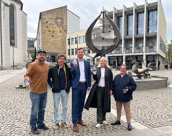 Fünf Personen vor einem Brunnen mit Handy in der Hand