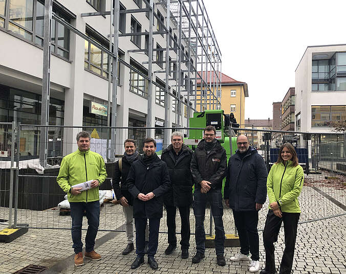 Männer und eine Frau stehen vor einem Stahlbaugerüst für eine Fassadenbegrünung