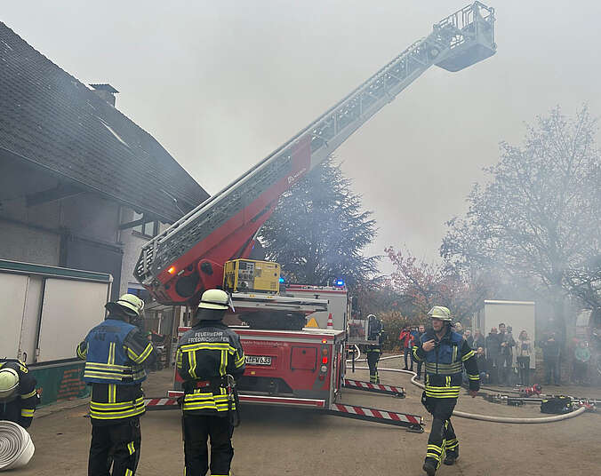 Eine Drehleiter mit Korb, viel Rauch und Einsatzkräfte der Feuerwehr in Uniformen löschen Brand