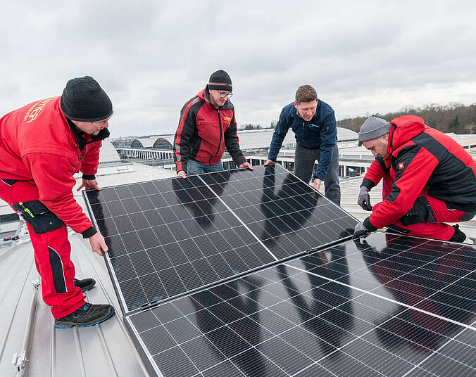 Vier Männer auf einem Dach montieren PV-Modul