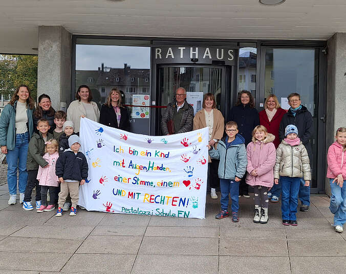 Kinder und Erwachsene vor dem Rathaus mit einem großen weißen Transparent