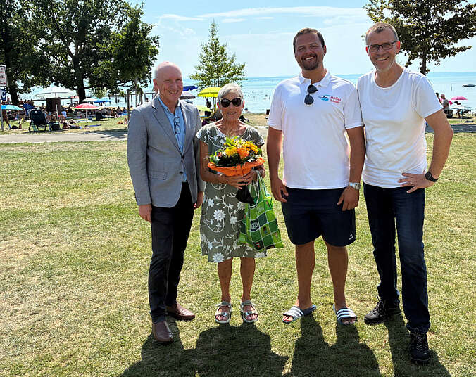 Drei Männer und eine Frau stehen auf der Wiese, im Hintergrund der Bodensee.
